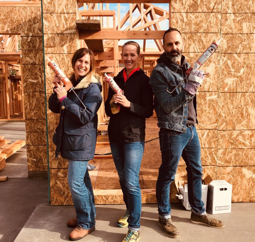 Volunteers from a community group pose with caulking guns on the construction site at Bend-Redmond Habitat for Humanity
